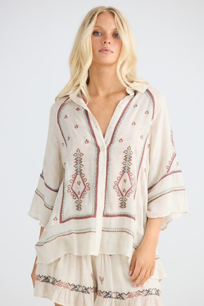 Woman wearing a cream-colored embroidered dress on a white background