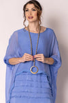 Woman wearing a blue dress with a long necklace against a plain background