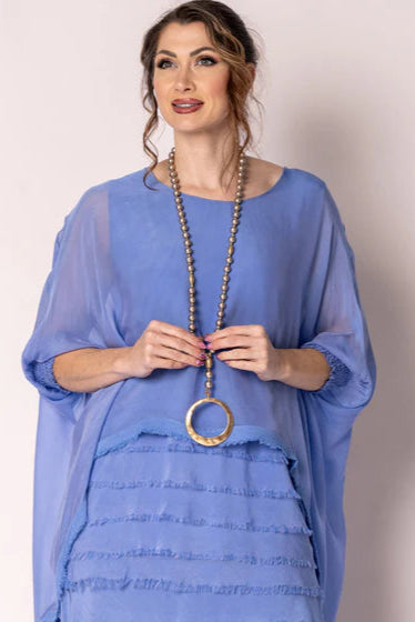 Woman wearing a blue dress with a long necklace against a plain background
