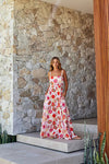 Woman in a floral dress standing on stone steps outside a modern building with stone and wooden walls.
