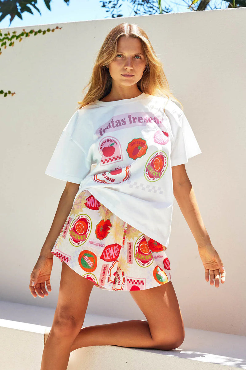 Woman wearing a white oversized t-shirt with colorful graphics and a matching skirt outdoors.