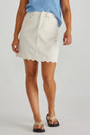 Person wearing a white denim skirt with scalloped hem on a plain background