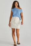 Woman wearing a blue top and white skirt on a plain background