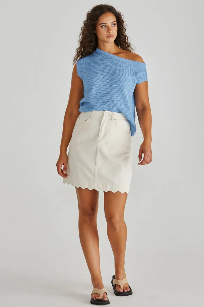 Woman wearing a blue top and white skirt on a plain background