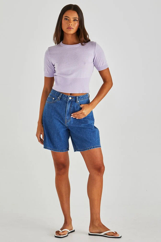 Woman wearing a light purple crop top and blue denim shorts on a white background