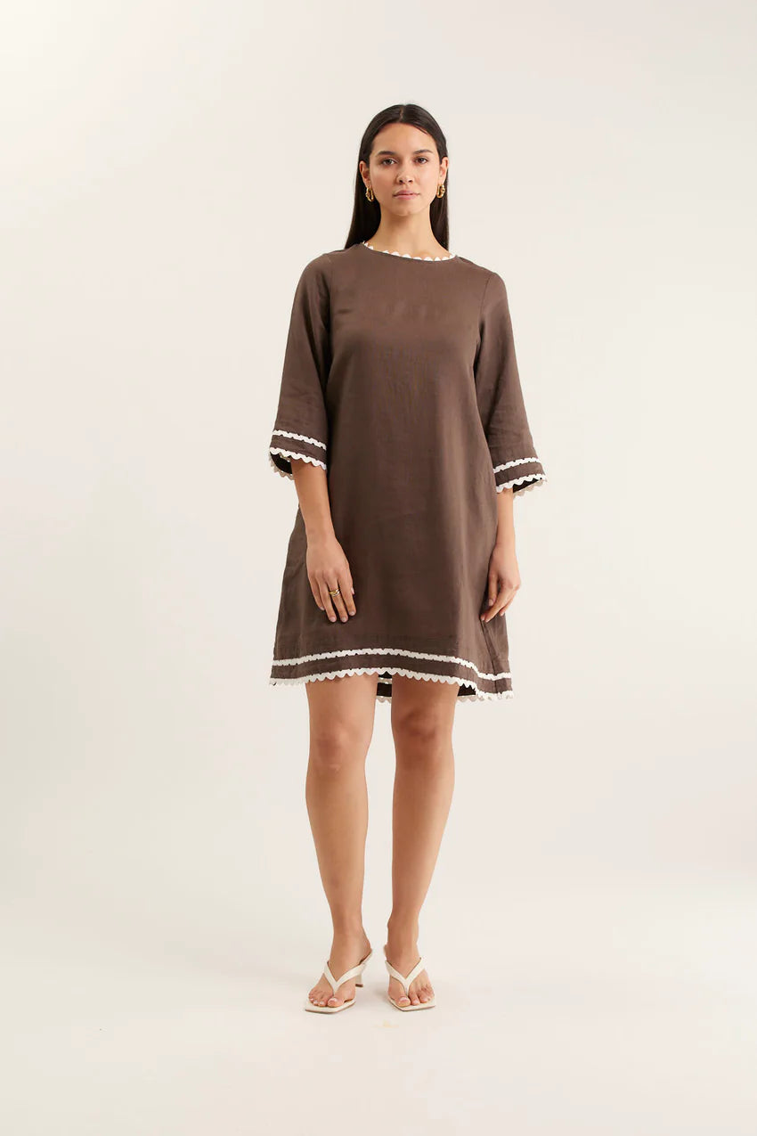 Woman wearing a brown dress with white trim on a white background