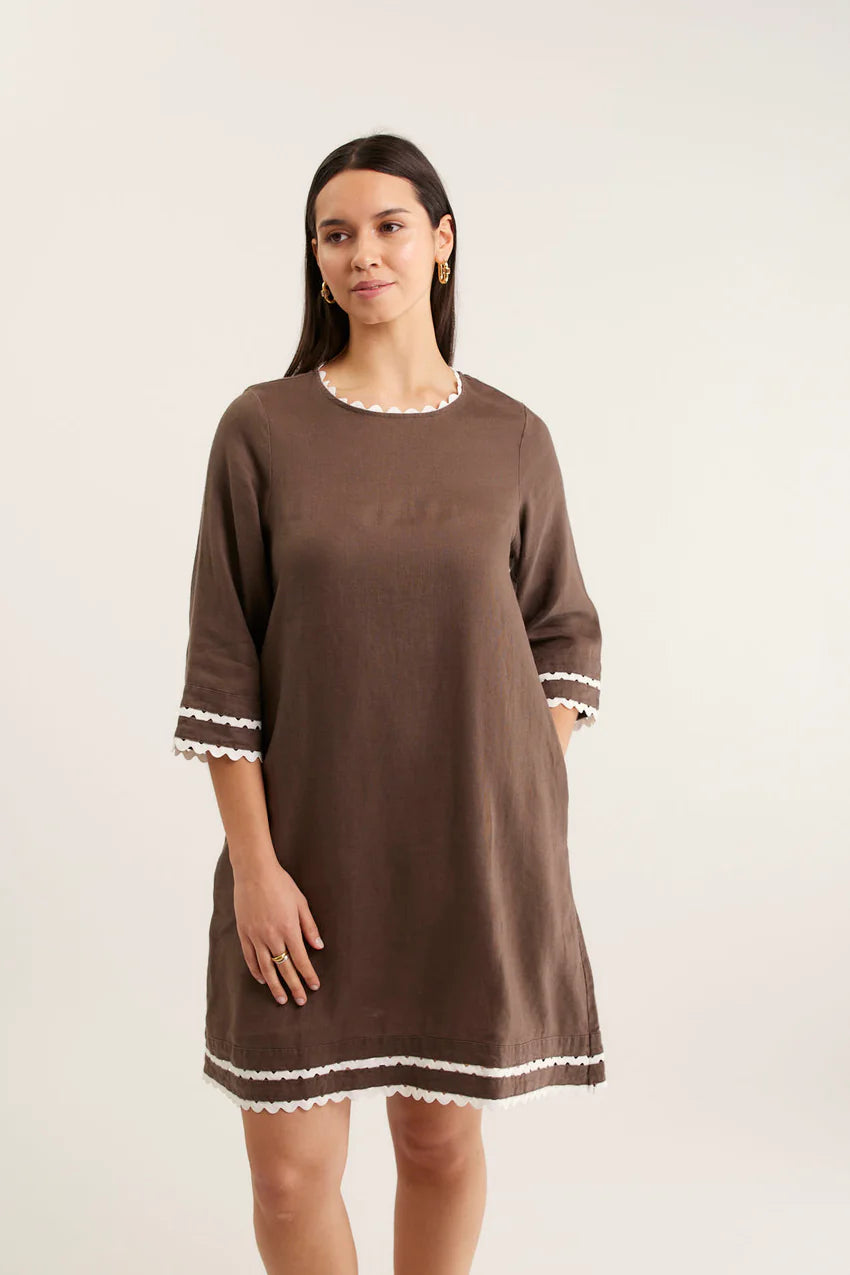 Woman wearing a brown dress with white trim on a plain background