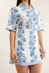 White dress with blue floral pattern worn by a person on a plain background