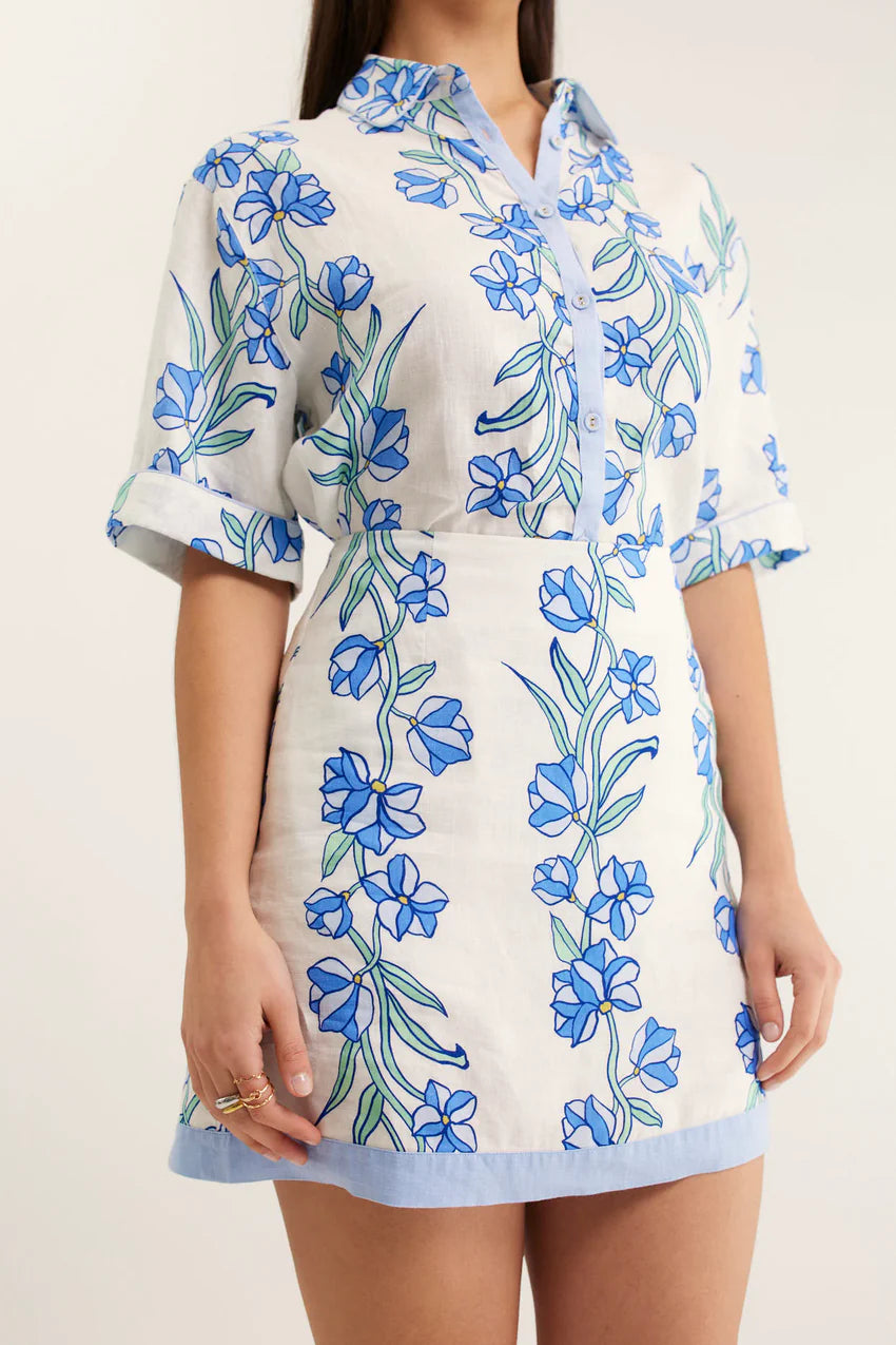 White dress with blue floral pattern worn by a person on a plain background
