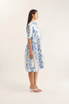 Woman wearing a white dress with blue floral pattern on a plain background