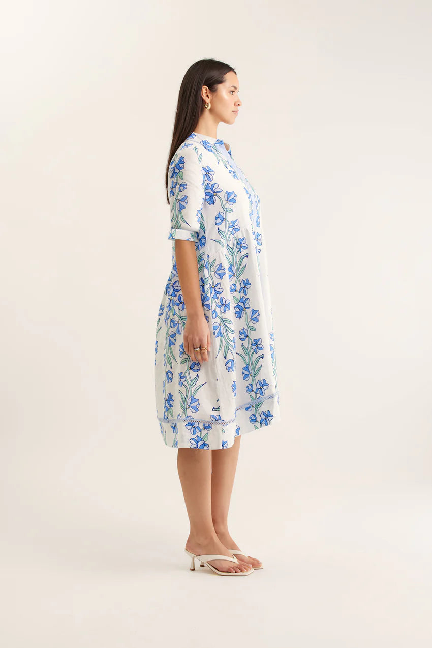 Woman wearing a white dress with blue floral pattern on a plain background