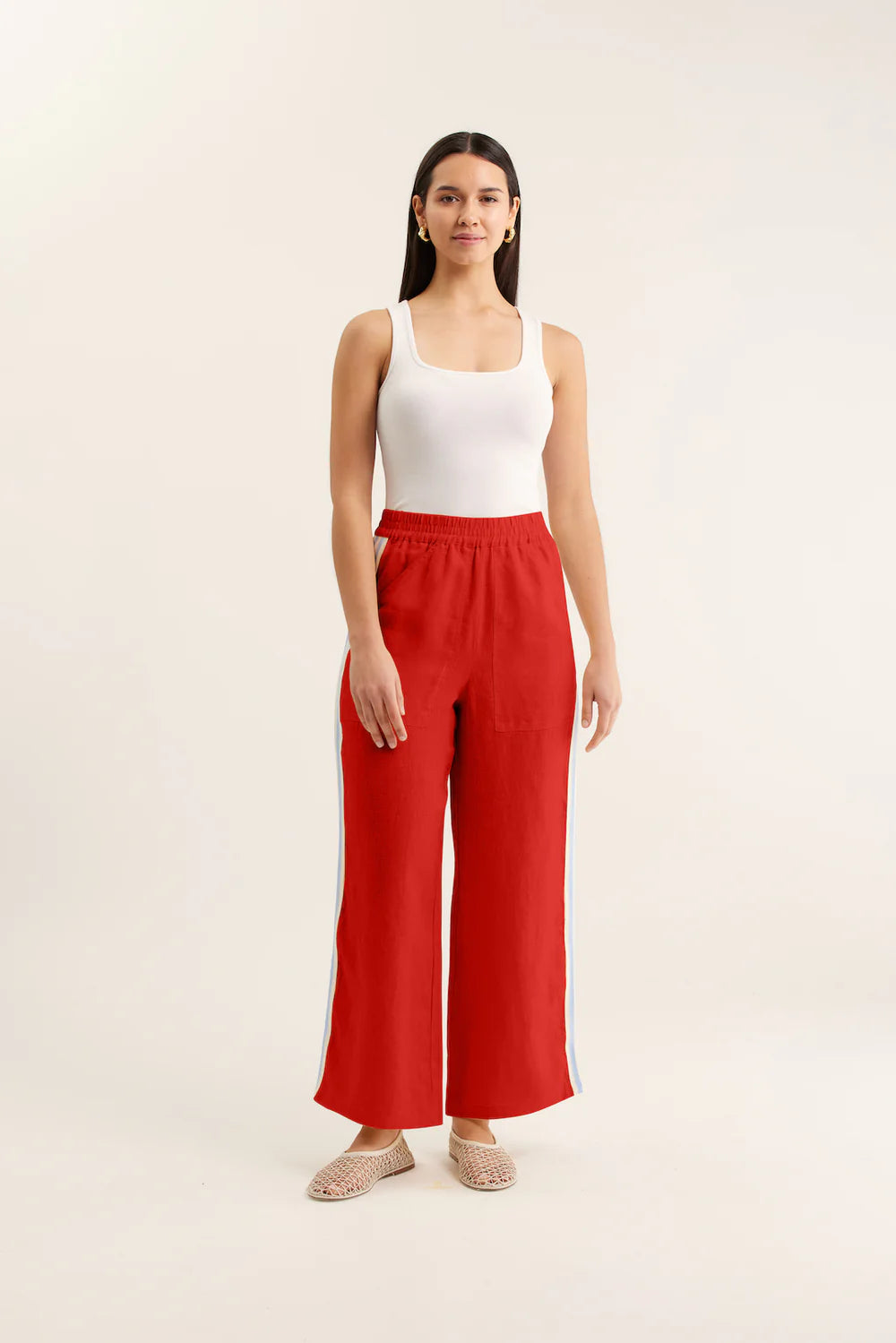 Woman wearing a white top and red pants on a beige background