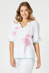Woman wearing a white cover-up with pink palm tree designs on a plain background