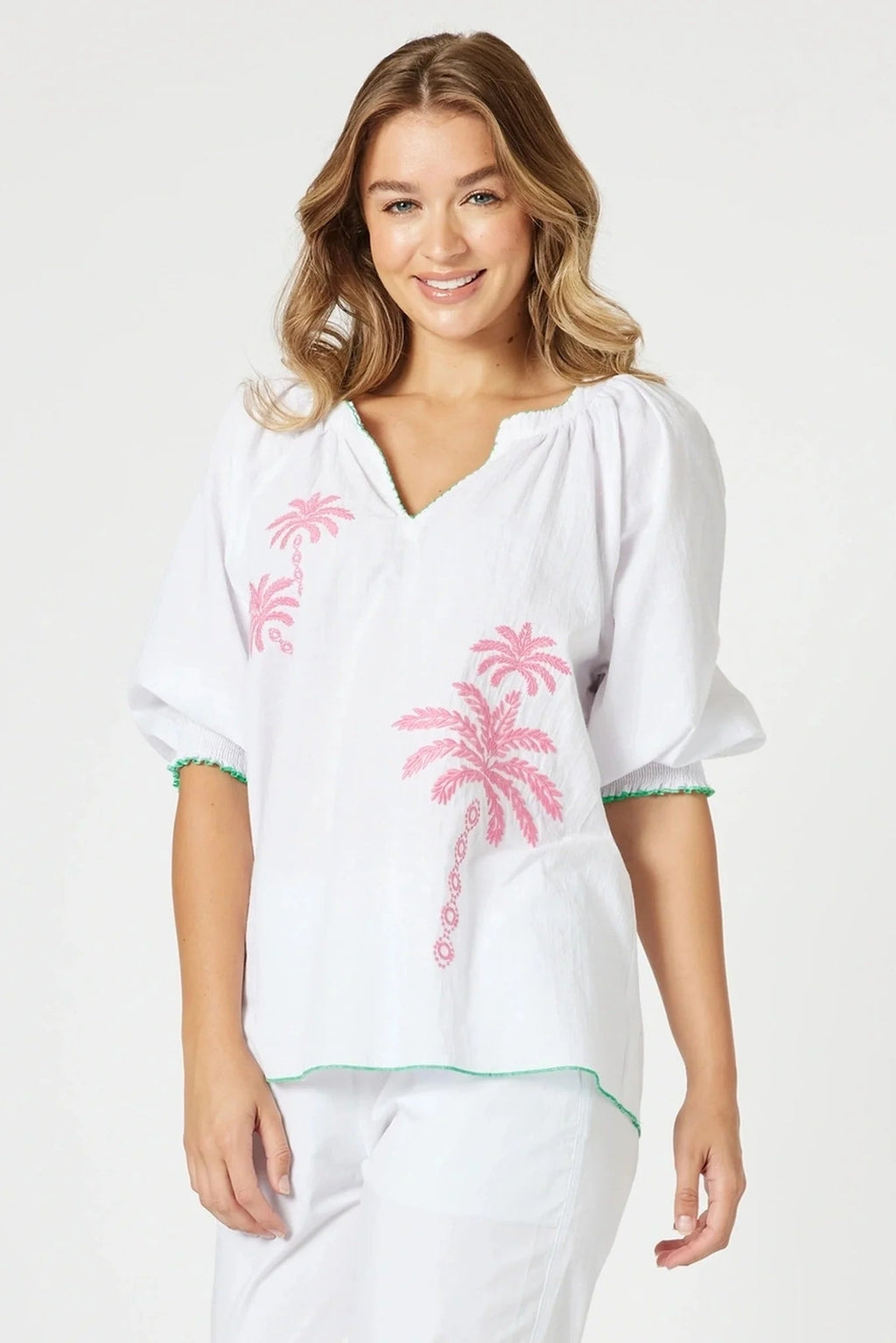 Woman wearing a white cover-up with pink palm tree designs on a plain background