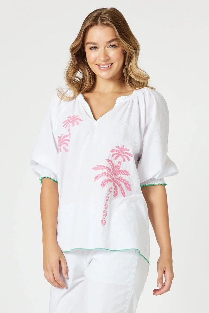 Woman wearing a white cover-up with pink palm tree designs on a plain background