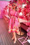 Woman in a pink dress standing in a vibrant, floral-themed outdoor setting.