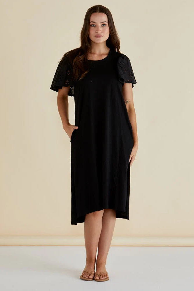 Woman wearing a black dress with ruffled sleeves against a beige background