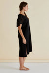 Woman wearing a black dress with lace sleeves against a beige background