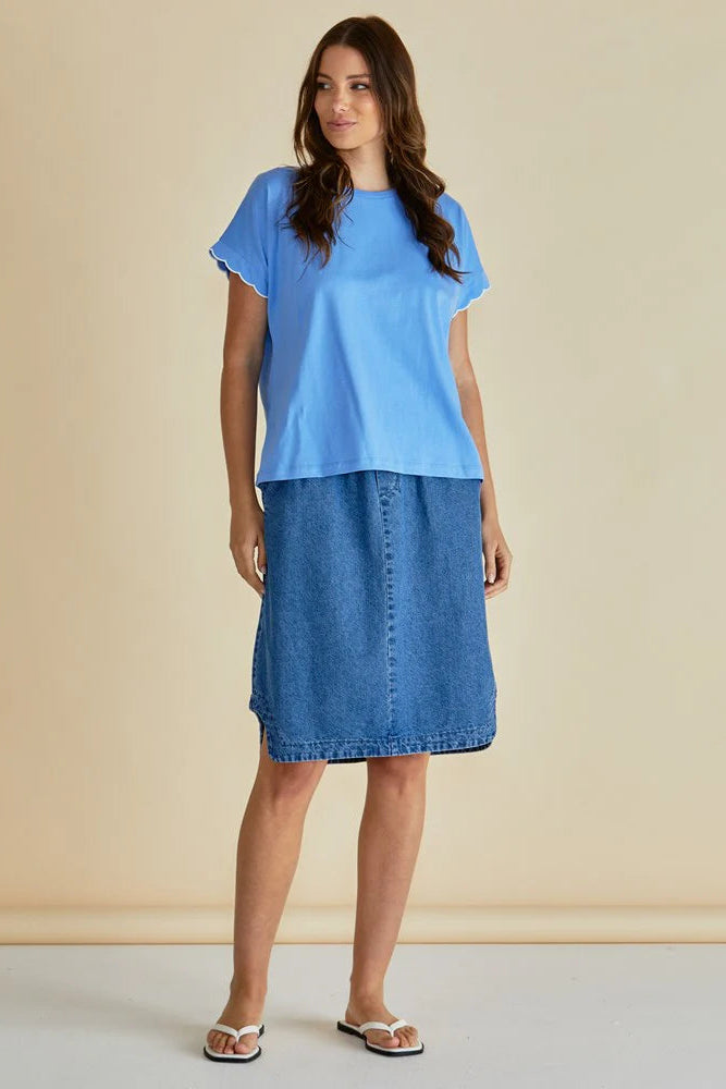 Woman wearing a blue top and denim skirt against a beige background