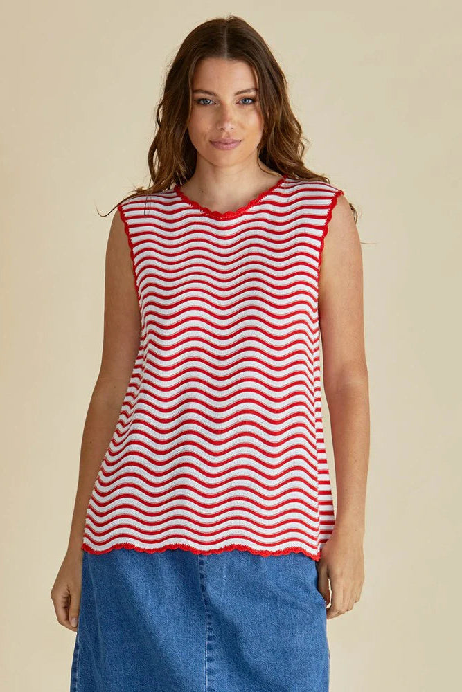 Woman wearing a red and white striped sleeveless top with blue jeans on a beige background