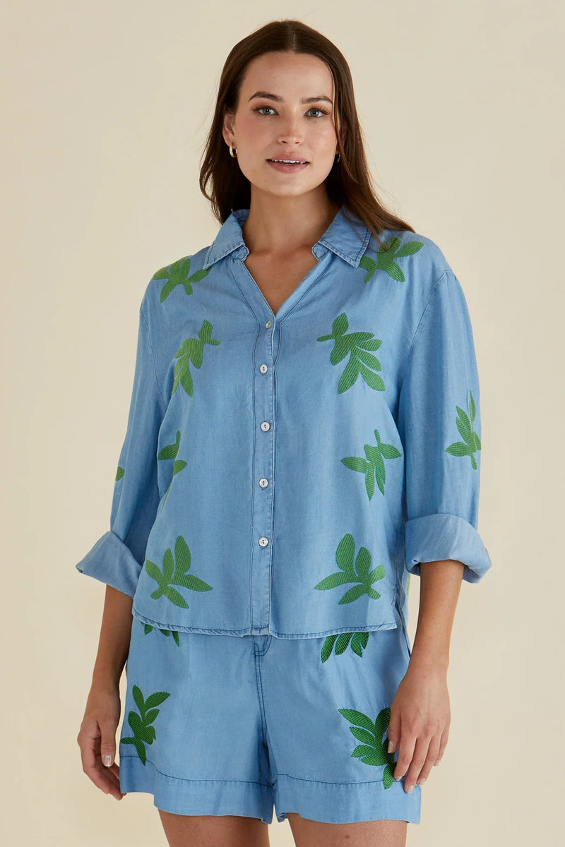 Woman wearing a blue shirt and shorts with green leaf patterns on a beige background