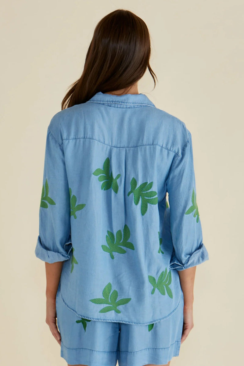 Woman wearing a blue denim outfit with green leaf patterns on a beige background