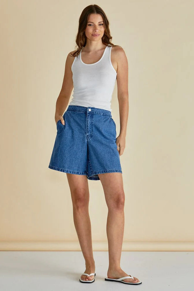 Woman wearing a white tank top and blue denim skirt against a beige background