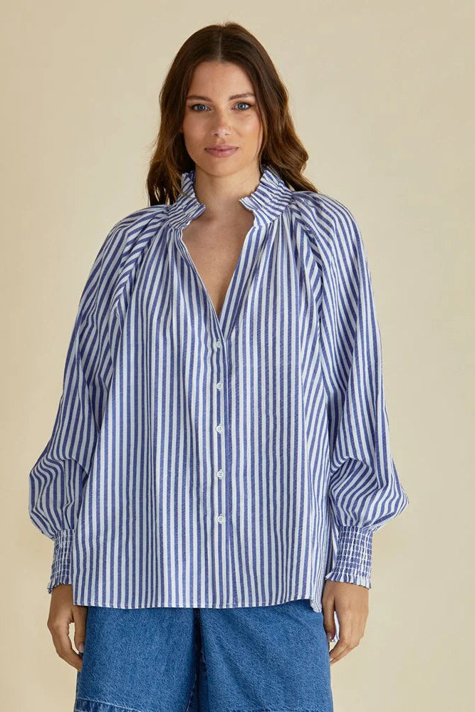 Woman wearing a blue and white striped shirt with rolled-up sleeves on a beige background