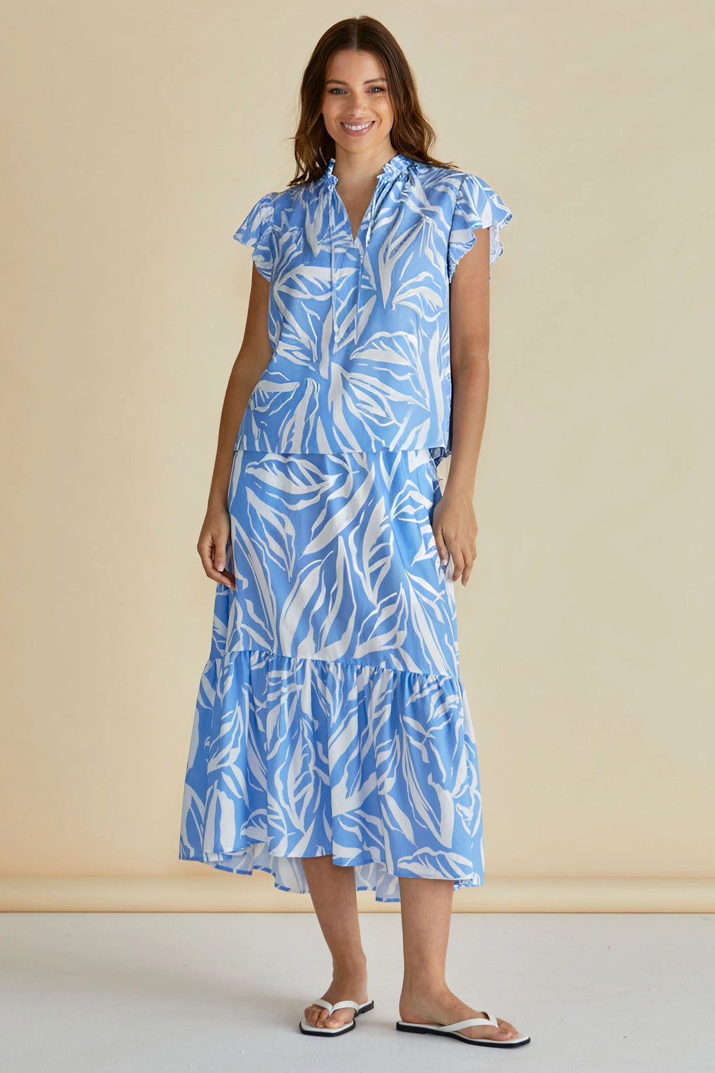 Woman wearing a blue and white leaf-patterned dress against a beige background