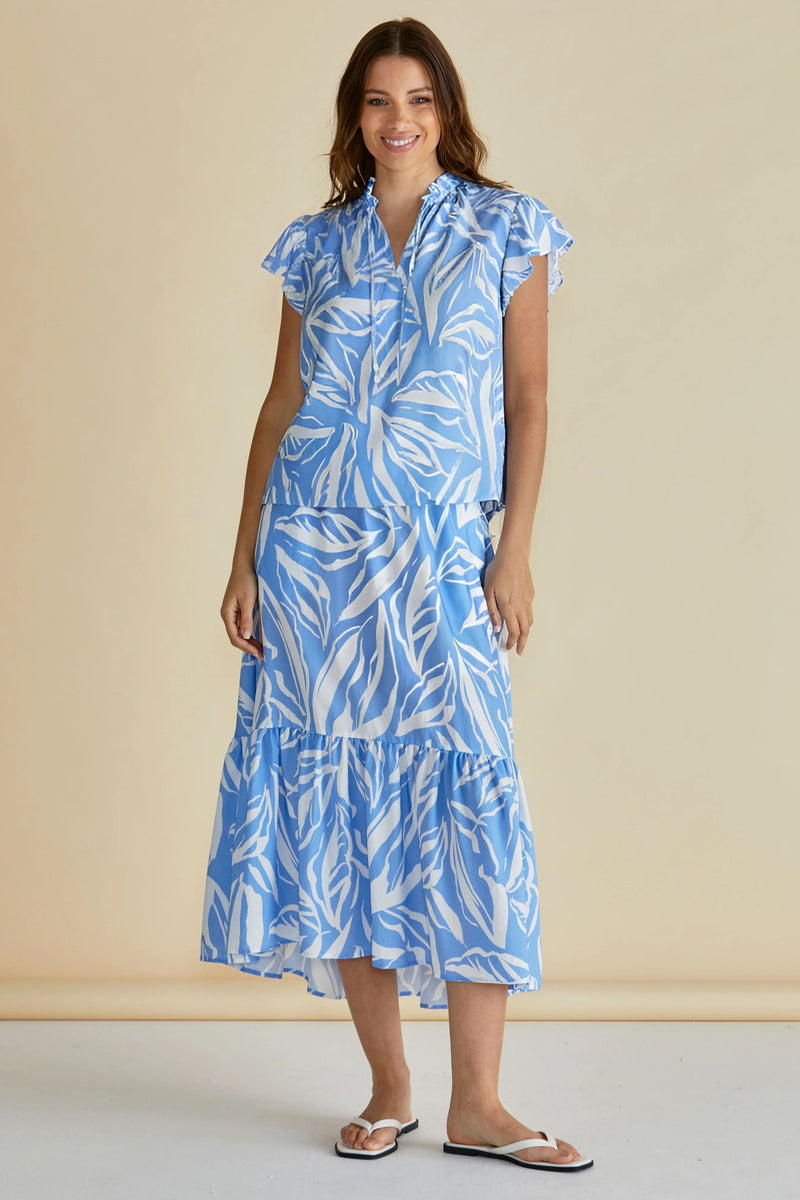 Woman wearing a blue and white leaf-patterned dress against a beige background