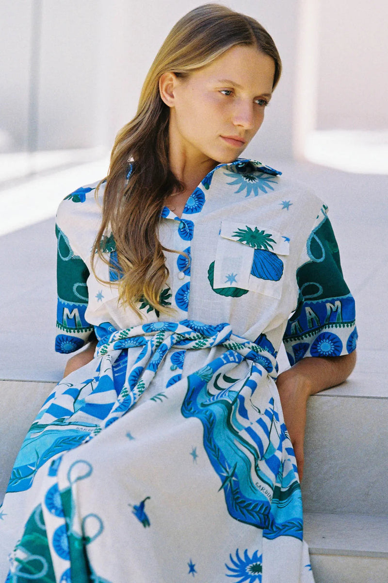Woman wearing a white dress with blue and green patterns sitting on a white surface.