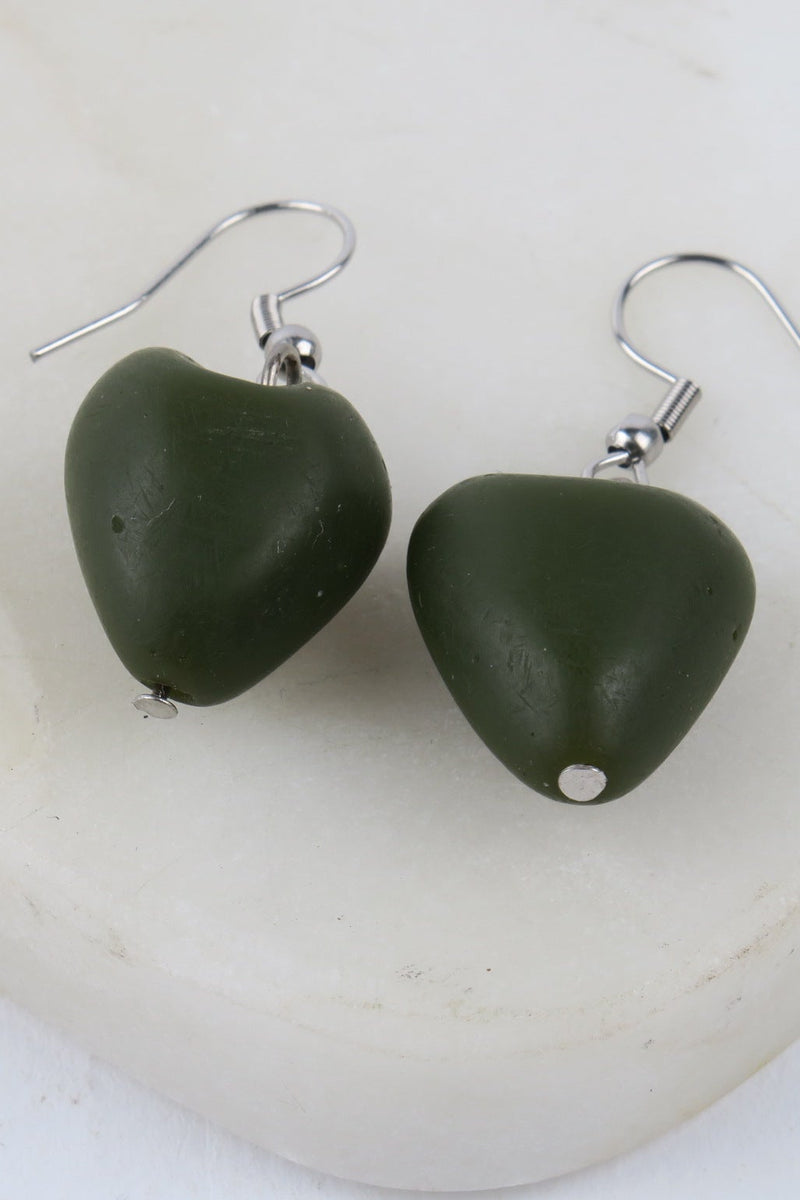 Green heart-shaped earrings on a white stone background