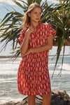 Woman wearing a red patterned dress standing on a beach with palm leaves in the background