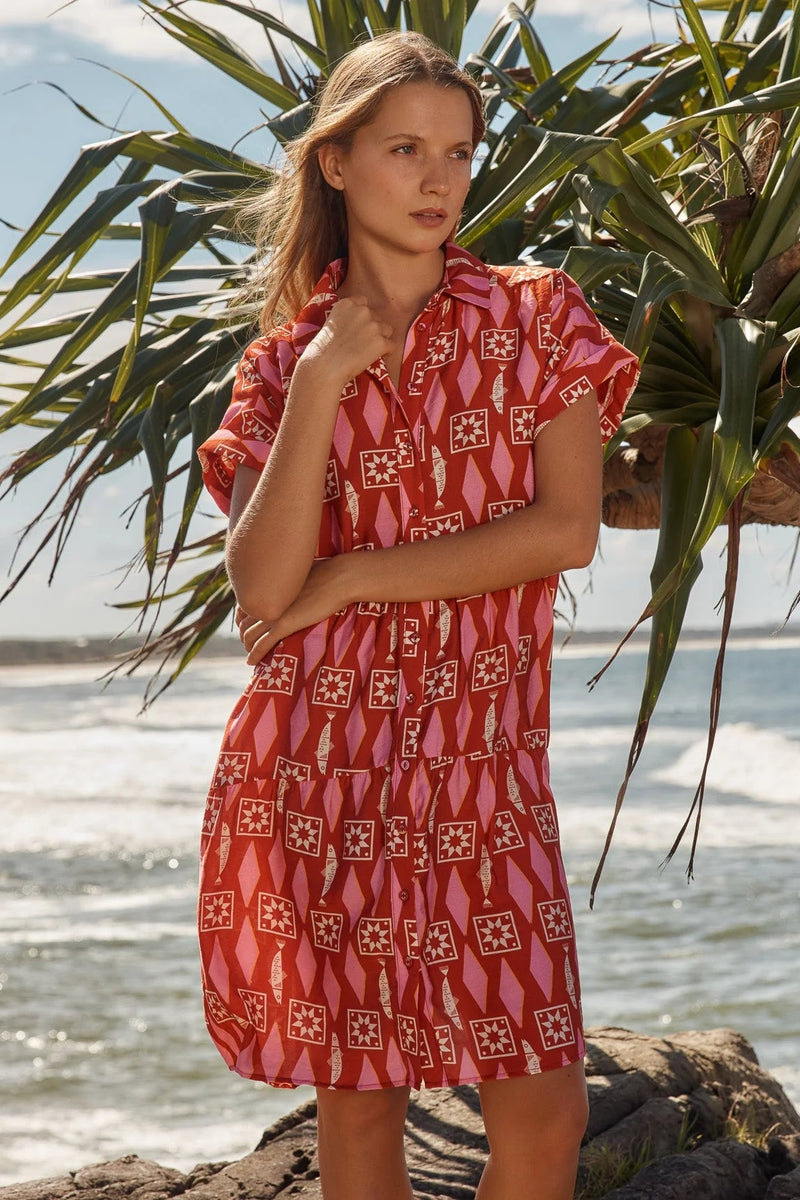 Woman wearing a red patterned dress standing on a beach with palm leaves in the background