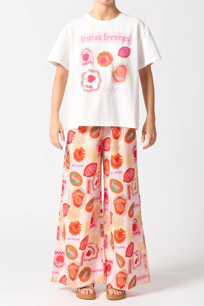 Person wearing a white t-shirt with fruit graphics and colorful patterned pants on a white background