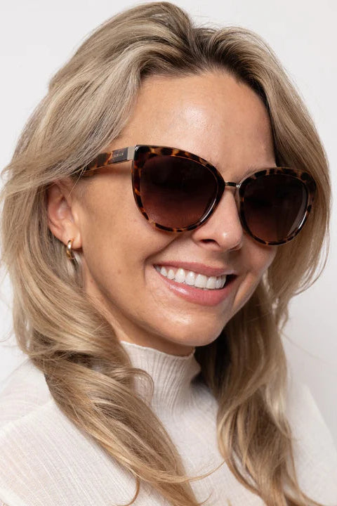 Woman wearing tortoiseshell sunglasses with a plain background