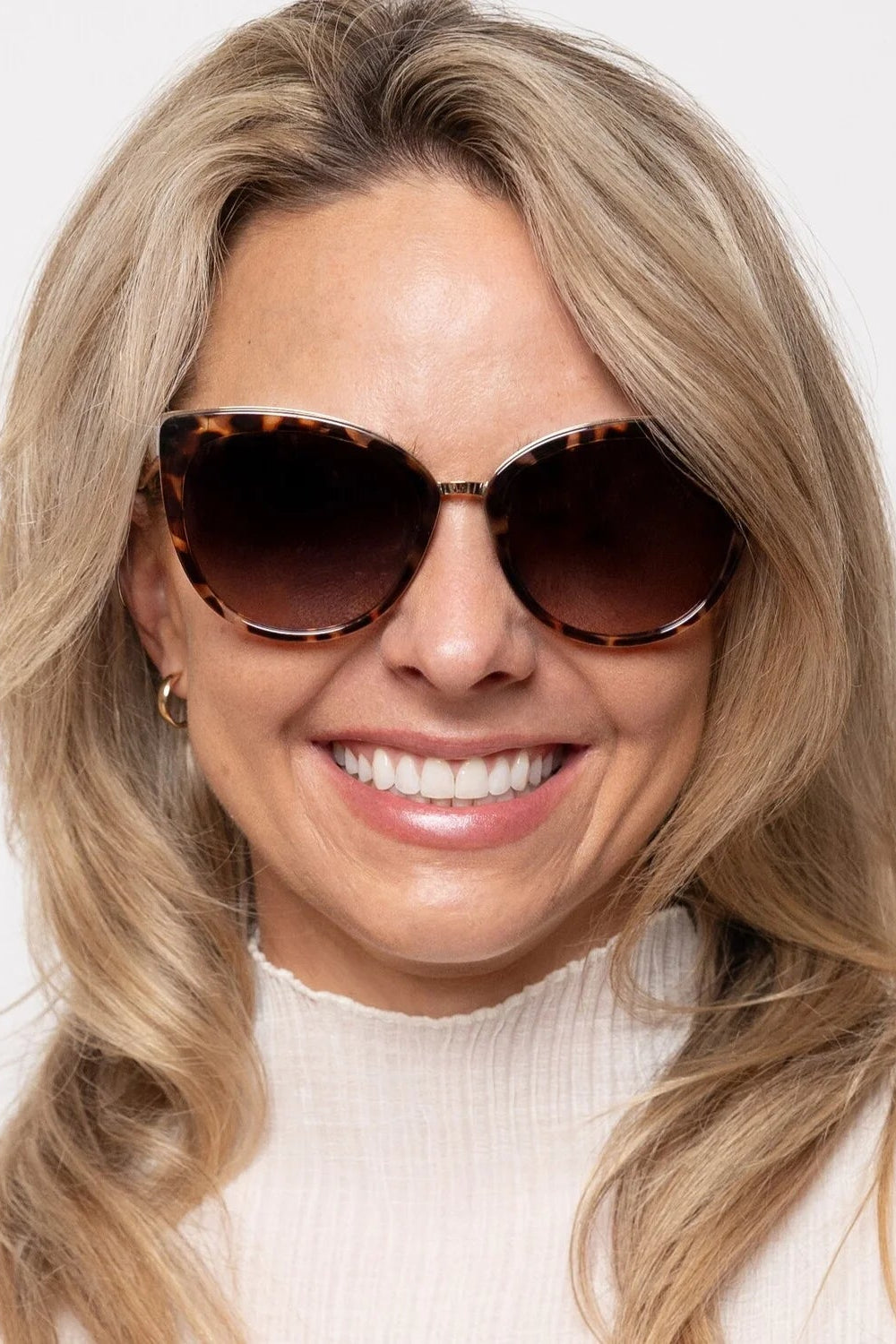 Woman wearing tortoiseshell sunglasses with a plain background