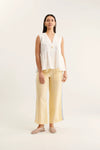 Woman wearing a white sleeveless top and yellow pants on a white background