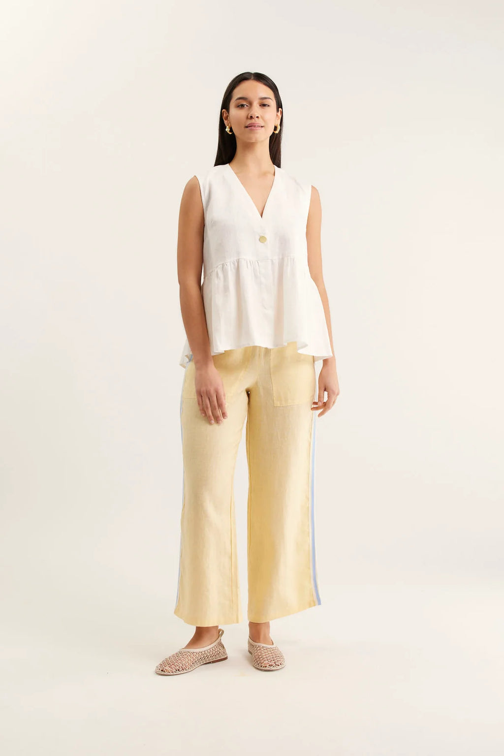 Woman wearing a white sleeveless top and yellow pants on a white background