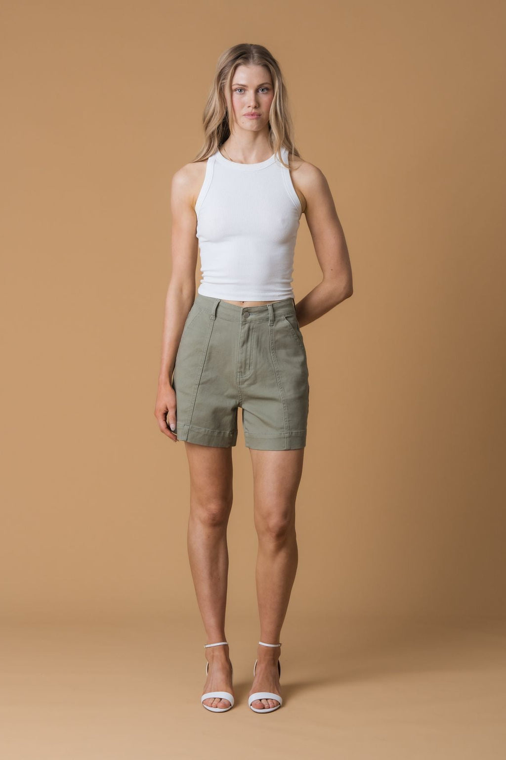 Woman wearing a white tank top and green shorts against a brown background