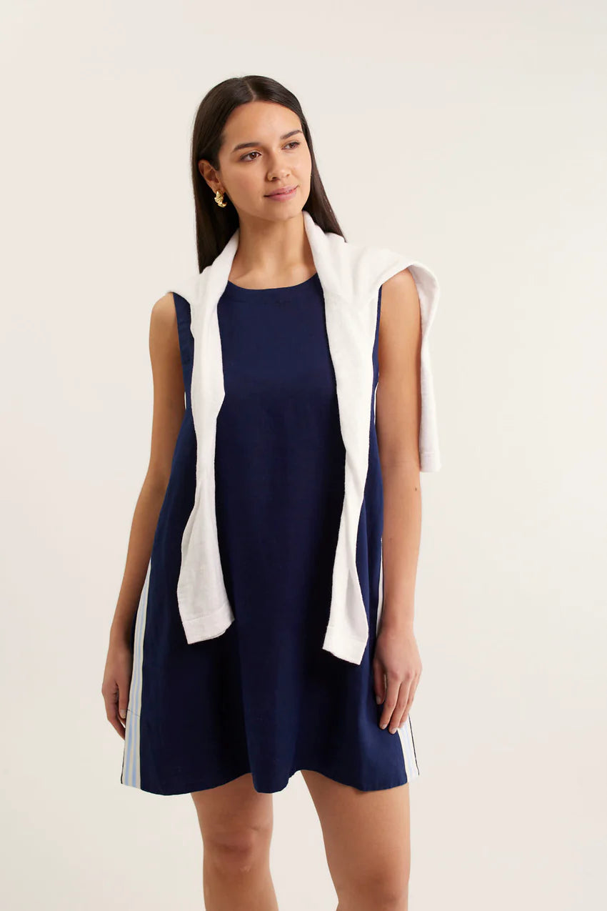 Woman wearing a navy dress with a white sleeveless jacket on a light background