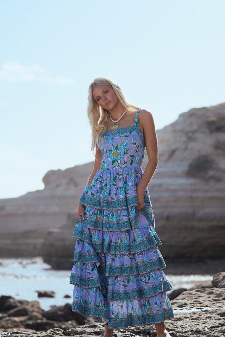 Woman in a blue floral dress standing on a rocky beach with cliffs in the background